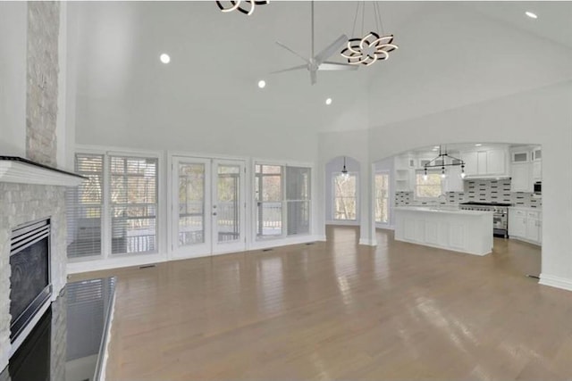 unfurnished living room featuring a chandelier, recessed lighting, wood finished floors, a glass covered fireplace, and high vaulted ceiling