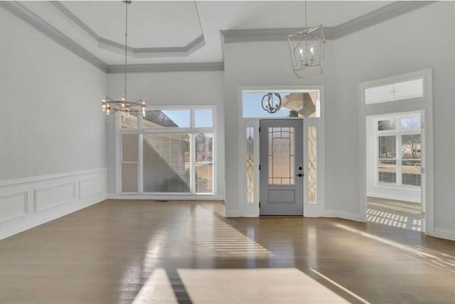 foyer entrance with a chandelier, crown molding, a high ceiling, wood finished floors, and a wainscoted wall