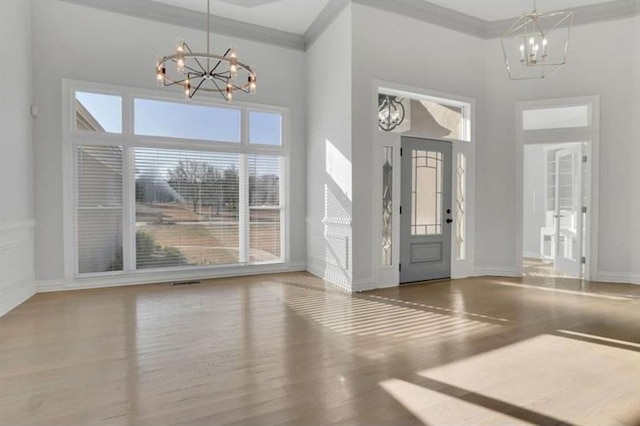 entryway with a chandelier, wood finished floors, a high ceiling, baseboards, and ornamental molding