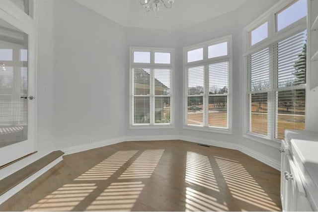 unfurnished sunroom with a chandelier, baseboards, and wood finished floors