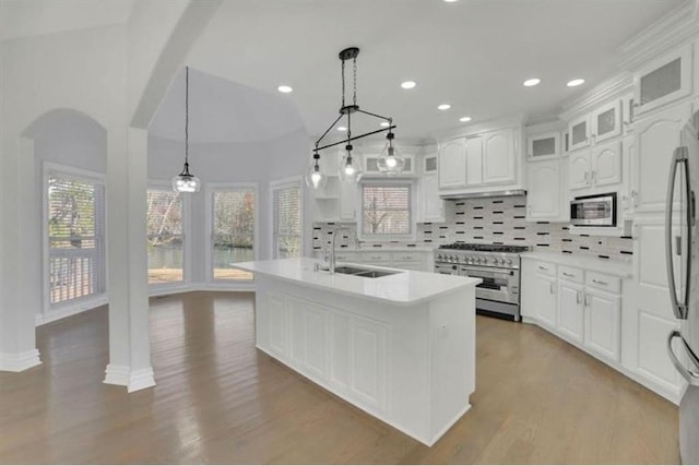 kitchen featuring stainless steel appliances, a sink, decorative backsplash, light countertops, and arched walkways