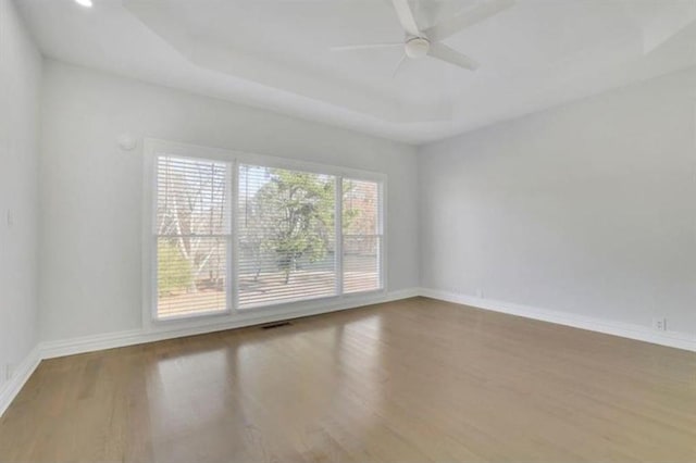 unfurnished room featuring a ceiling fan, wood finished floors, baseboards, visible vents, and a tray ceiling