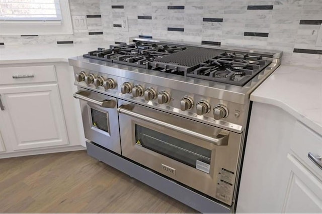 kitchen view of range with two ovens, backsplash, light countertops, white cabinetry, and light wood-style floors