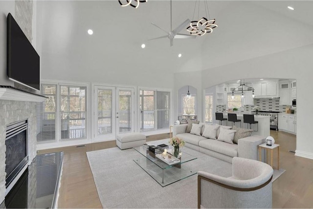 living area featuring recessed lighting, ceiling fan with notable chandelier, light wood-style floors, a glass covered fireplace, and high vaulted ceiling