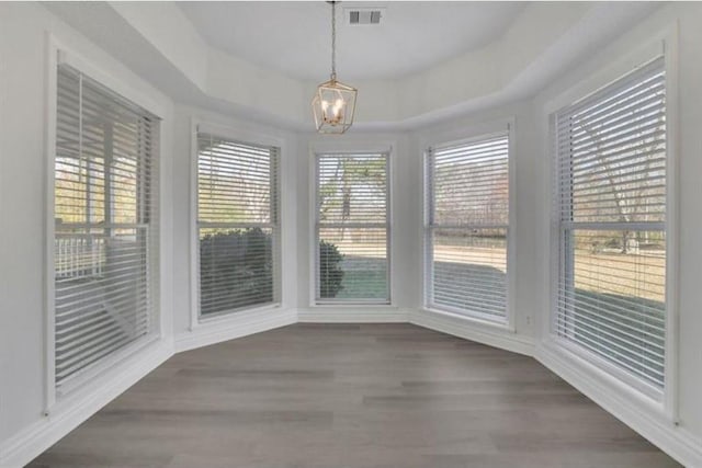 unfurnished dining area with a tray ceiling, visible vents, wood finished floors, and a chandelier