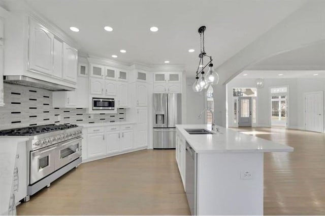 kitchen featuring stainless steel appliances, a sink, arched walkways, backsplash, and white cabinetry