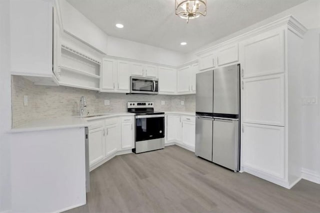 kitchen featuring light wood finished floors, backsplash, appliances with stainless steel finishes, white cabinetry, and a sink