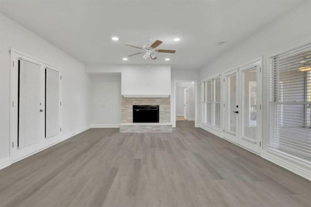 unfurnished living room with a fireplace with raised hearth, a ceiling fan, wood finished floors, recessed lighting, and baseboards