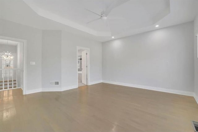 empty room with ceiling fan, wood finished floors, a chandelier, a tray ceiling, and baseboards