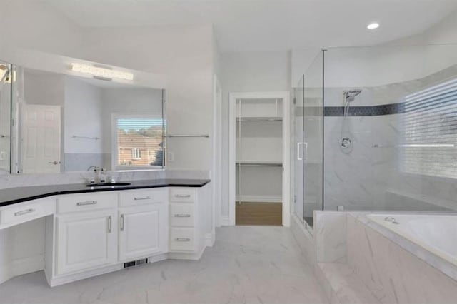 full bath featuring a shower stall, marble finish flooring, a garden tub, vanity, and a walk in closet