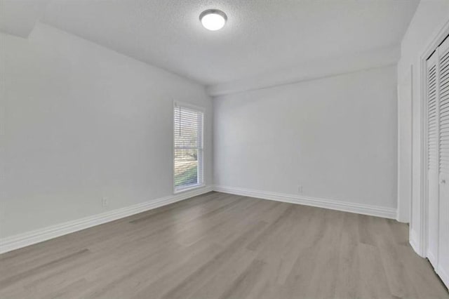 unfurnished bedroom featuring wood finished floors, baseboards, a closet, and a textured ceiling