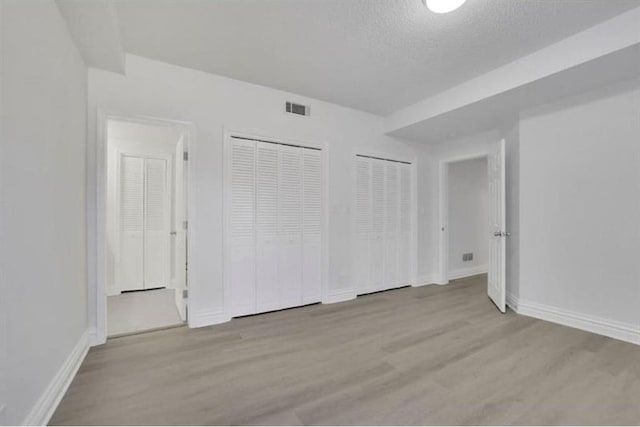unfurnished bedroom with two closets, wood finished floors, and baseboards