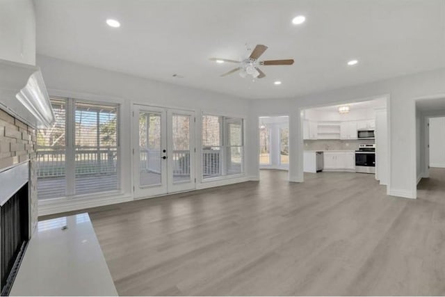 unfurnished living room featuring a fireplace, a ceiling fan, light wood finished floors, baseboards, and french doors
