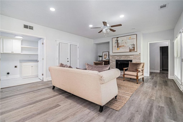 living room featuring ceiling fan, light wood-type flooring, a stone fireplace, baseboards, and recessed lighting