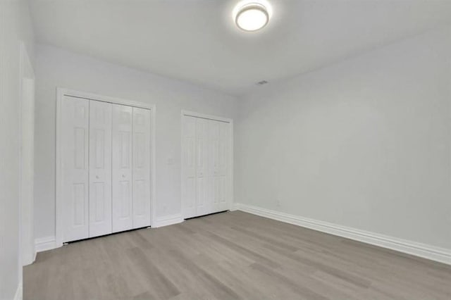 unfurnished bedroom with wood finished floors, two closets, and baseboards