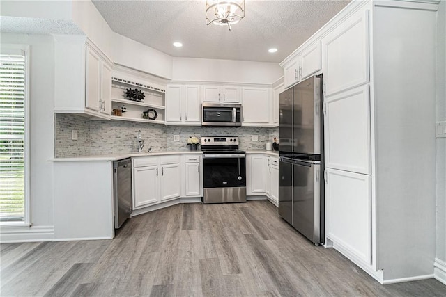kitchen with appliances with stainless steel finishes, light wood-style flooring, a textured ceiling, open shelves, and decorative backsplash