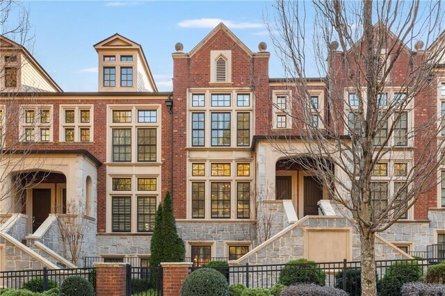 view of front facade featuring a fenced front yard, stone siding, stairs, and brick siding