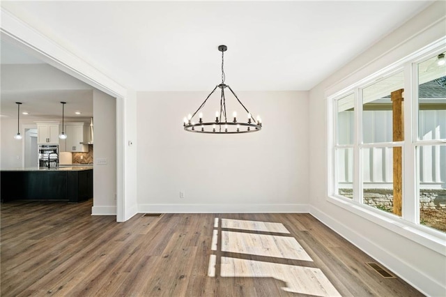 unfurnished dining area with wood-type flooring and an inviting chandelier