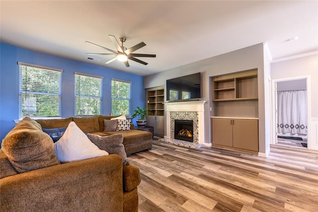 living room with ceiling fan, light hardwood / wood-style flooring, built in features, and ornamental molding