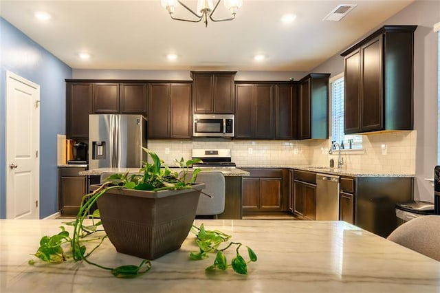 kitchen featuring appliances with stainless steel finishes, decorative backsplash, an inviting chandelier, and light stone counters