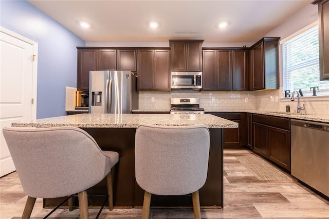 kitchen with light wood-type flooring, a kitchen island, light stone countertops, and stainless steel appliances