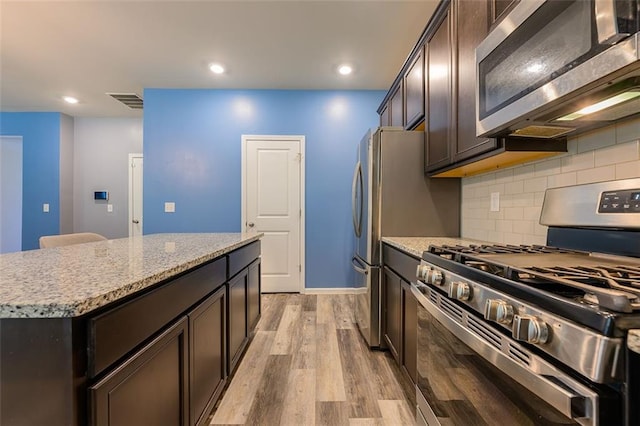 kitchen with appliances with stainless steel finishes, light hardwood / wood-style floors, a kitchen island, and light stone counters