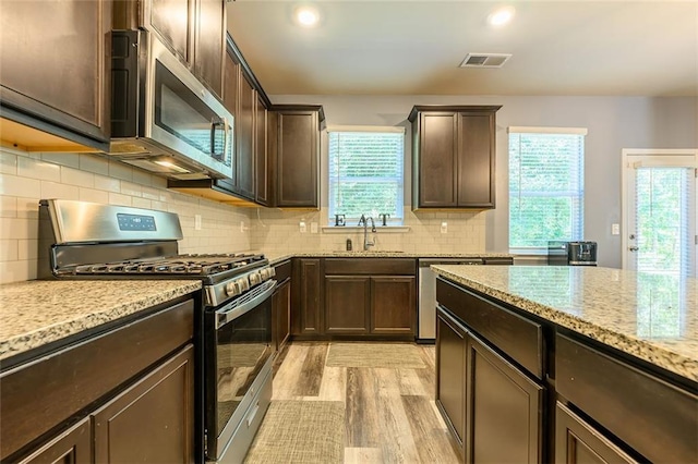 kitchen featuring dark brown cabinets, light stone counters, light hardwood / wood-style floors, backsplash, and appliances with stainless steel finishes