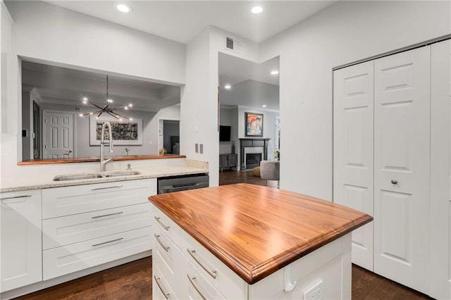 kitchen featuring decorative light fixtures, white cabinetry, an inviting chandelier, sink, and light stone counters