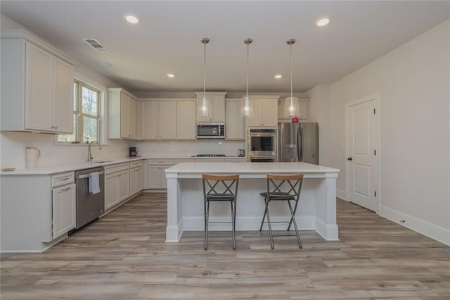 kitchen with stainless steel appliances, a sink, a kitchen island, visible vents, and light wood-type flooring