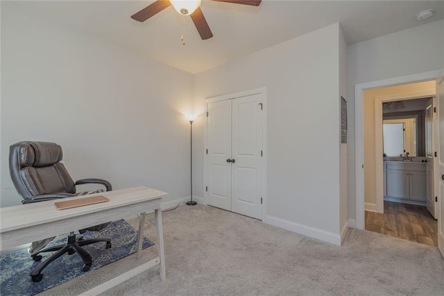 carpeted office space with a ceiling fan and baseboards