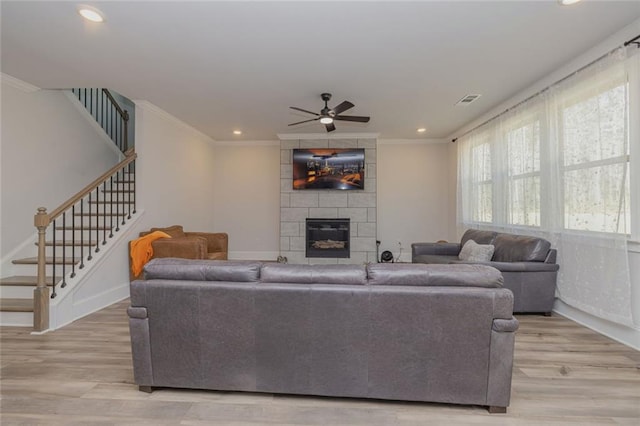 living area featuring light wood-style floors, a tile fireplace, crown molding, and stairs