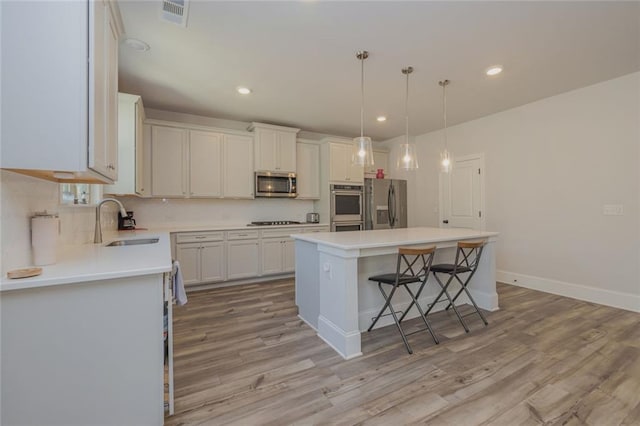 kitchen featuring visible vents, a breakfast bar area, a center island, stainless steel appliances, and a sink