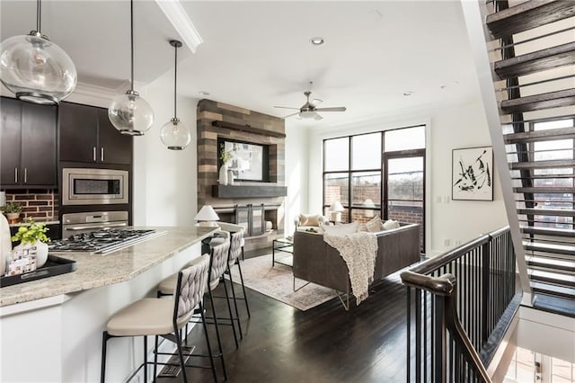 kitchen with stainless steel microwave, backsplash, dark wood-style floors, a breakfast bar area, and crown molding