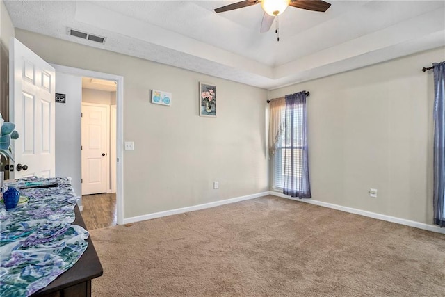 bedroom with a raised ceiling, carpet, and ceiling fan