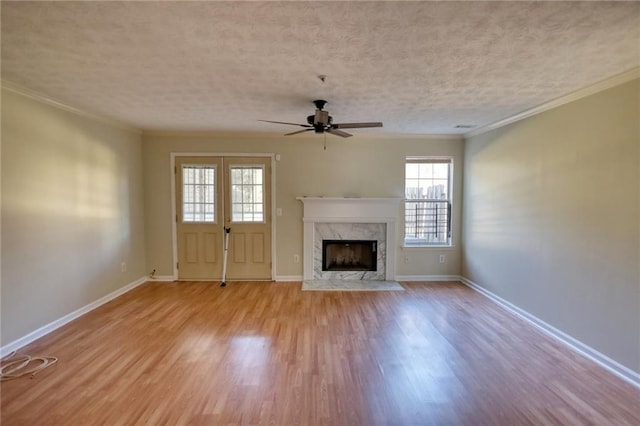 unfurnished living room featuring ceiling fan, a high end fireplace, crown molding, light hardwood / wood-style floors, and a textured ceiling