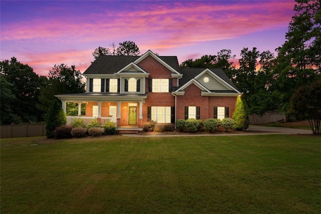 colonial home featuring a lawn, fence, covered porch, concrete driveway, and brick siding