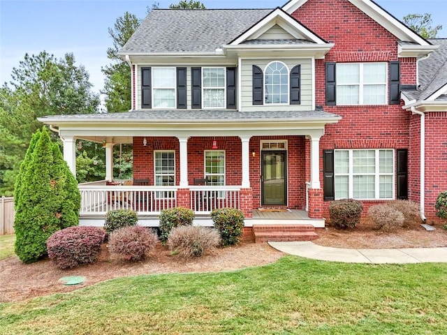 view of front of home featuring a front lawn, brick siding, covered porch, and roof with shingles