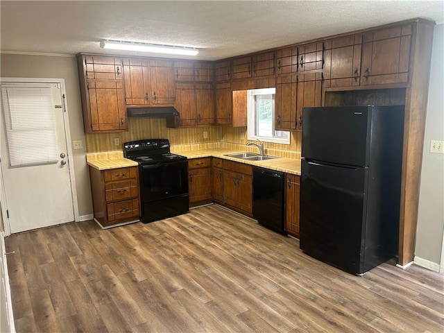 kitchen with light countertops, a sink, under cabinet range hood, and black appliances