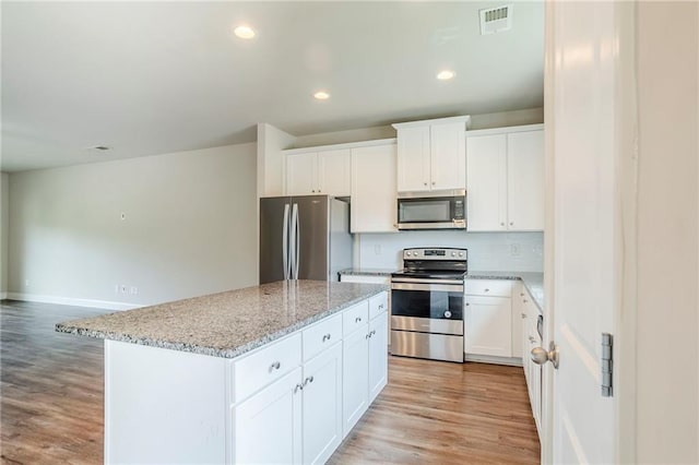 235 Orchard Dr, Covington, GA 30014 - kitchen featuring stainless steel appliances, light wood-type flooring, a kitchen island, light stone countertops, and backsplash