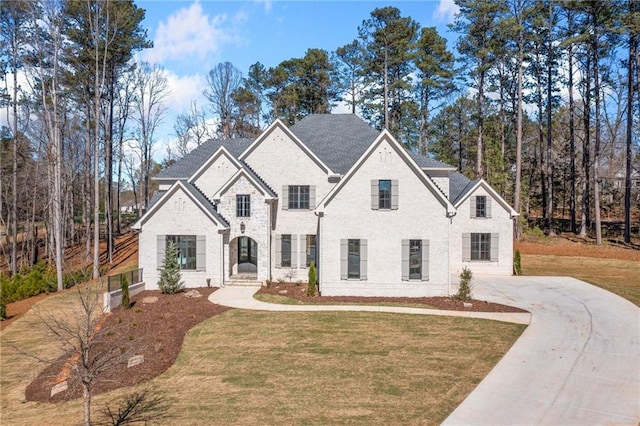 french country style house with driveway, a front yard, and brick siding