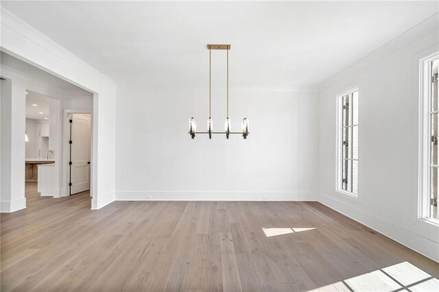 unfurnished dining area with baseboards, a notable chandelier, crown molding, and light wood-type flooring