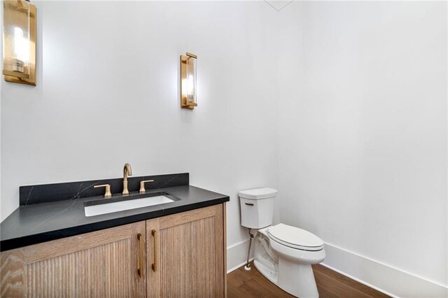 half bath with baseboards, toilet, vanity, and wood finished floors