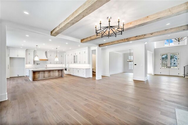 unfurnished living room with recessed lighting, an inviting chandelier, baseboards, beamed ceiling, and light wood finished floors