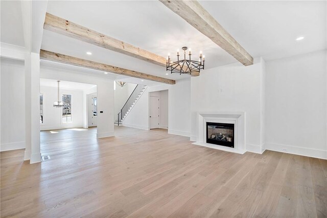 unfurnished living room with stairs, a notable chandelier, light wood-style flooring, and beamed ceiling