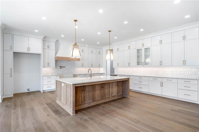 kitchen with light countertops, light wood finished floors, white cabinetry, custom range hood, and a large island with sink