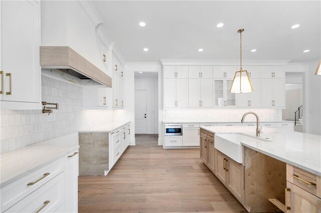 kitchen with ornamental molding, a sink, light wood-type flooring, and light stone counters