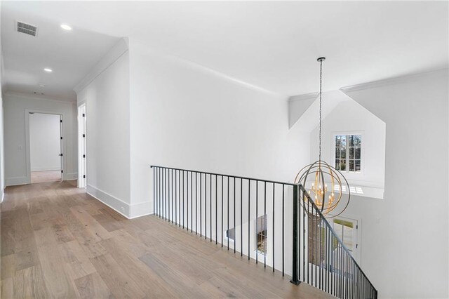 hall featuring a notable chandelier, crown molding, wood finished floors, baseboards, and visible vents