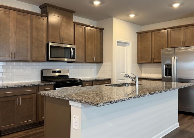 2277 Whitworth St, Lawrenceville, GA 30044 - kitchen featuring appliances with stainless steel finishes, a sink, dark stone counters, dark wood-style floors, and an island with sink