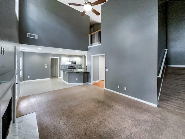 unfurnished living room featuring a towering ceiling, light colored carpet, sink, and ceiling fan