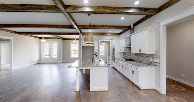 kitchen featuring pendant lighting, french doors, a center island with sink, white cabinets, and light stone counters